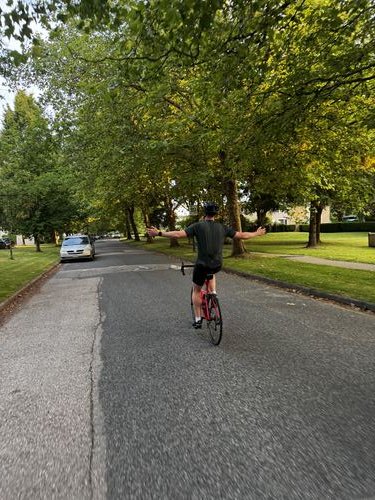 Ezrah riding his road bike down a tree-lined street